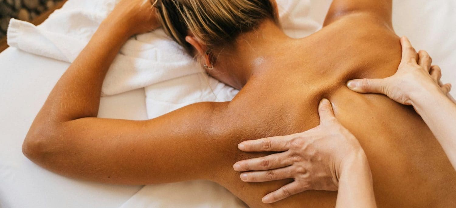 Handen die met rustige, lange halen de rug en schouder masseren