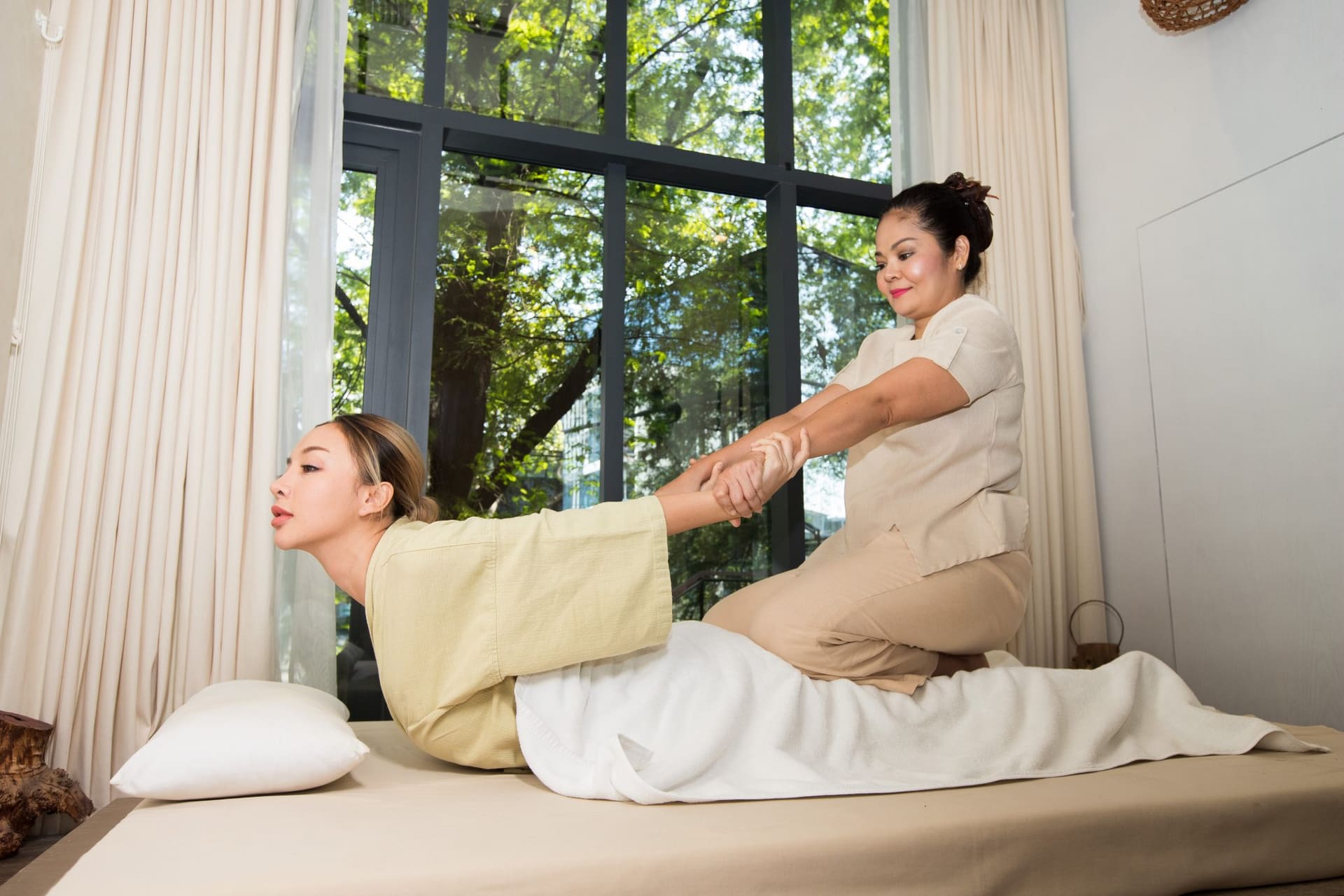Masseuse strekt rustig de armen van een cliënt op de massagetafel tijdens een traditionele Thaise massage
