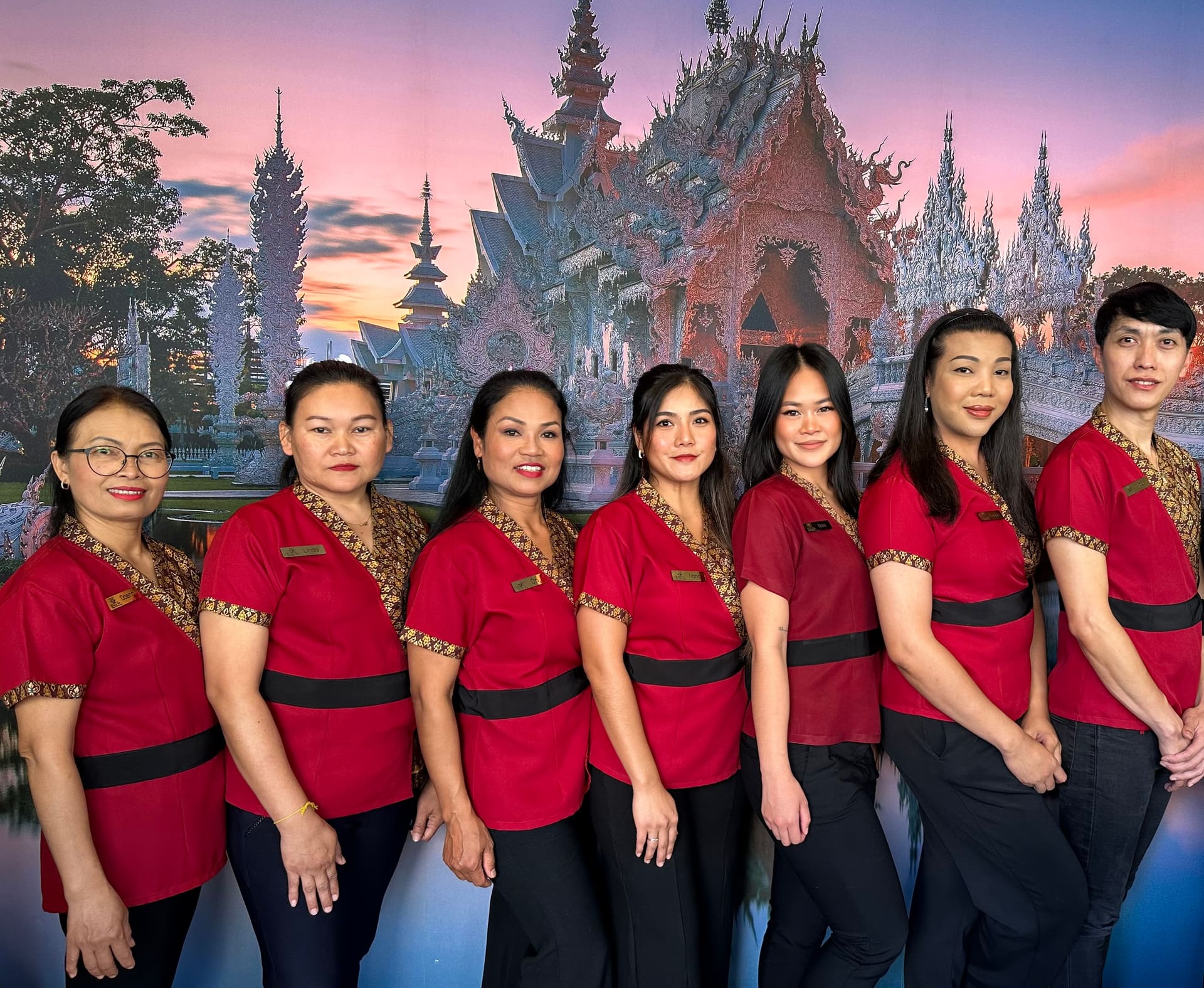 Het team van Bang-on Thai massage in rode uniformen voor een afbeelding van een Thaise tempel